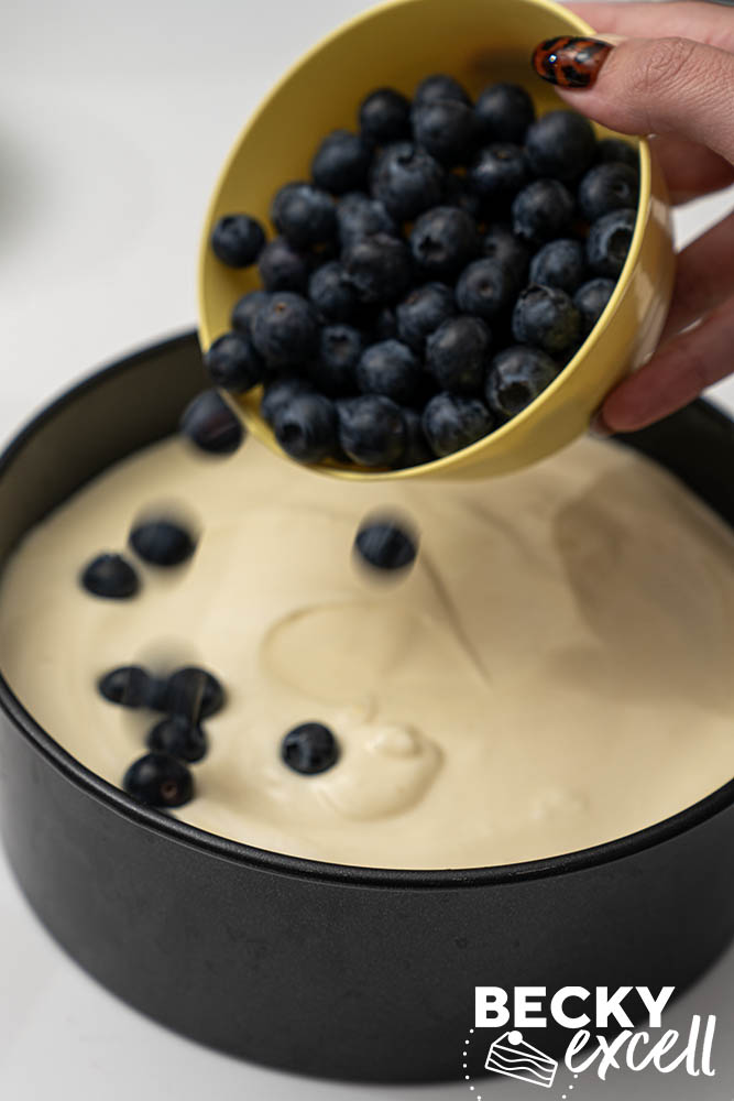 Adding the blueberries to the cheesecake filling once it has been filled half way