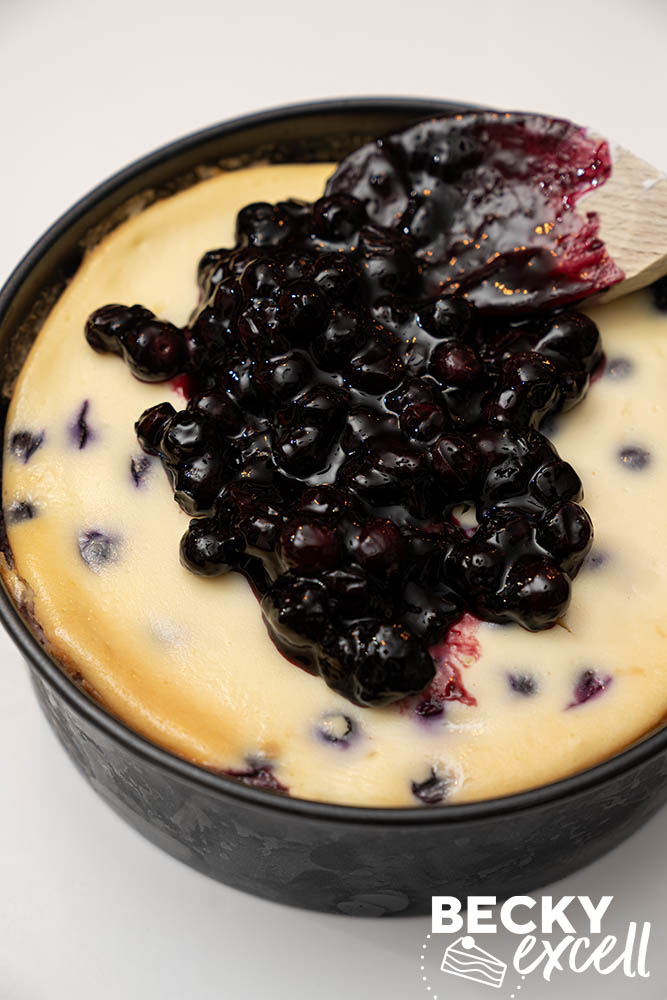 Spreading the blueberry filling on top of the fully cooled gluten-free baked blueberry cheesecake