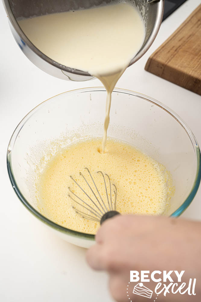 Adding the warm cream, milk and vanilla mixture to the caster sugar and egg yolks while whisking